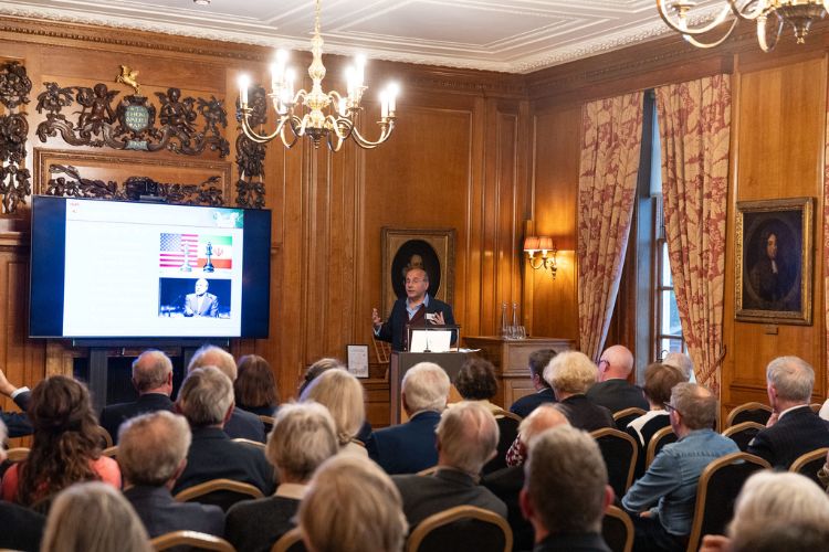 A male professor gives a talk to a seated audience in a wood-panelled room